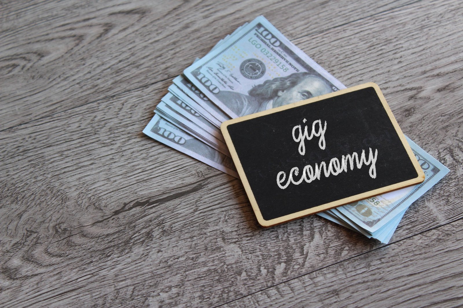 Chalkboard with text GIG ECONOMY on top of money with copy space.